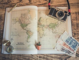 Atlas du monde ouvert sur une table. Caméra SLR noir et argent et billets de banques déposés sur l’atlas.