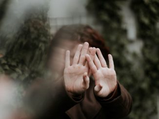 Personne en chemise à manches longues brunes couvrant le visage avec le dos des mains. L’image est floue, sauf pour les mains et les manches.