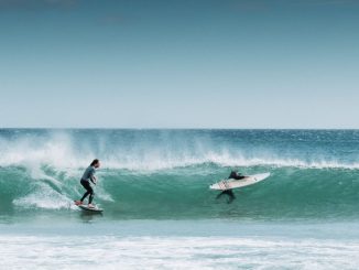 Deux hommes surfant sur les vagues de la mer durant le jour. Ciel complètement dégagé.
