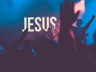 Concert religieux joué par un groupe sur scène. Jésus, affiché en très gros caractères blancs, apparaît au fond de la scène faiblement éclairée.
