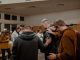 Des gens en vestes noires et marron debout devant d’autres gens pour prier dans une salle.