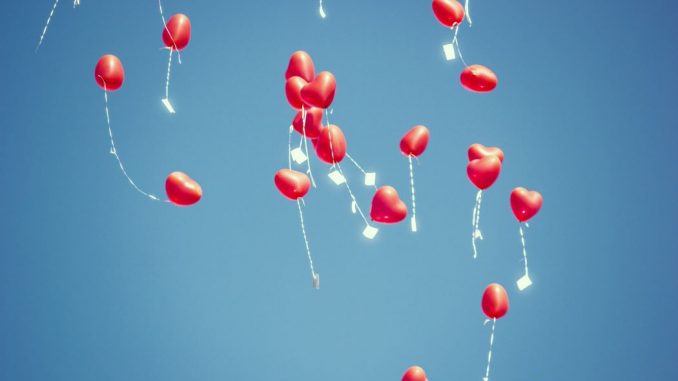 Lot de ballons en forme de cœur rouge sous un ciel bleu sans nuages.