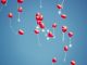 Lot de ballons en forme de cœur rouge sous un ciel bleu sans nuages.