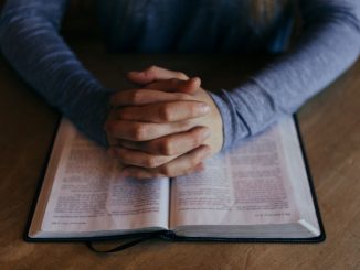 Homme les mains jointes sur une Bible ouverte. On voit seulement les avant-bras.