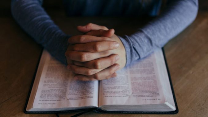 Homme les mains jointes sur une Bible ouverte. On voit seulement les avant-bras.