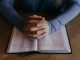 Homme les mains jointes sur une Bible ouverte. On voit seulement les avant-bras.