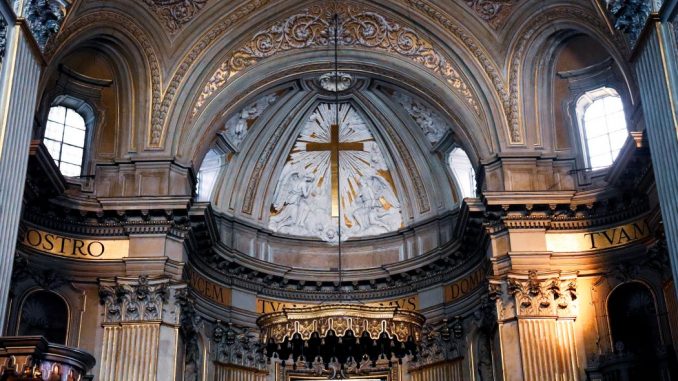 Gros plan de l’intérieur d’une cathédrale. On voit la partie haute du chœur et la croix centrale.