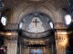 Gros plan de l’intérieur d’une cathédrale. On voit la partie haute du chœur et la croix centrale.