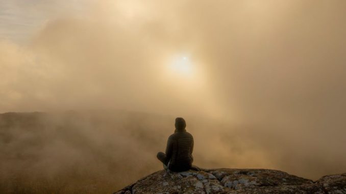 Personne assise sur un rocher durant la journée. Ciel brumeux.