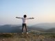 Homme en t-shirt blanc et pantalon gris debout au sommet d’une montagne.