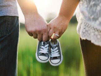 Femme et homme tenant des chaussures de berceau debout près de l’herbe verte pendant la journée.