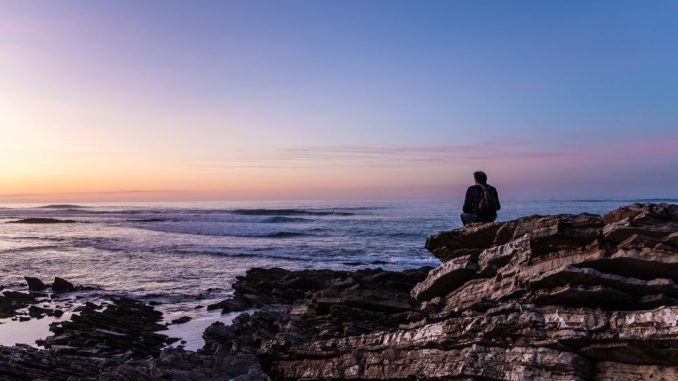Personne assise sur une falaise en bord de mer à la tombée du jour.