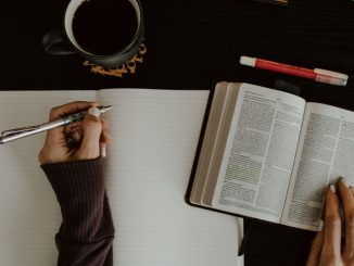 Personne qui prend des notes sur un papier blanc en étudiant la bible.