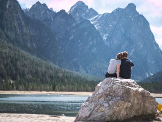 Un couple est assis sur un rocher face à un lac.