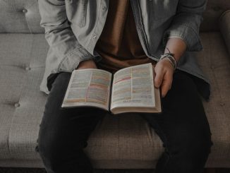 Personne avec une veste grise en jean lisant la bible.