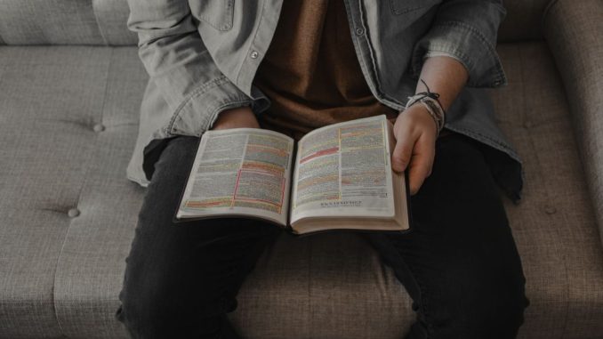 Personne avec une veste grise en jean lisant la bible.