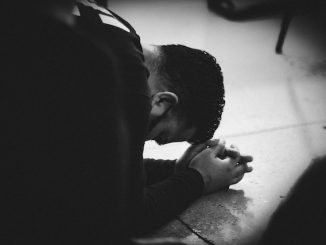 Homme en veste noire allongé sur le sol en prière.