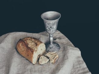 Morceau de pain près d’un gobelet sur une table avec nappe.