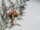 A brown wooden crucifix (take the cross) on a gray wall with flowers.