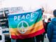 Group of people demonstrating for peace (good deeds). Peace flag in the foreground and other flags and signs behind, fog in the sky in the background.