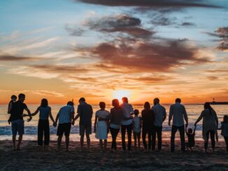 Large family united by love (love in your families), standing side by side on the beach, facing the sea and the setting sun on the horizon. Blue sky with red tinted clouds near the sun.