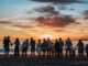 Large family united by love (love in your families), standing side by side on the beach, facing the sea and the setting sun on the horizon. Blue sky with red tinted clouds near the sun.