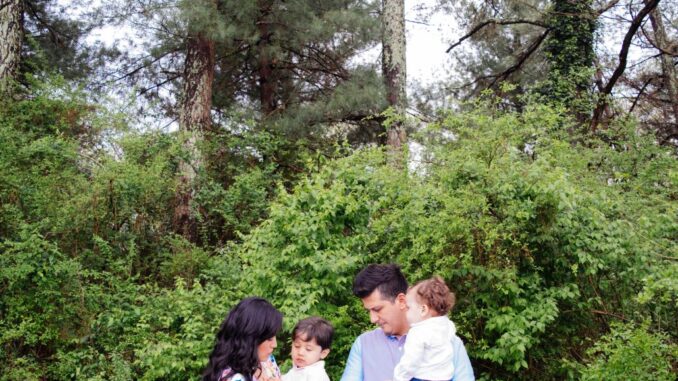 A father and a mother, each with a child in their arms, praying near a wooded area (renew prayer in your families).