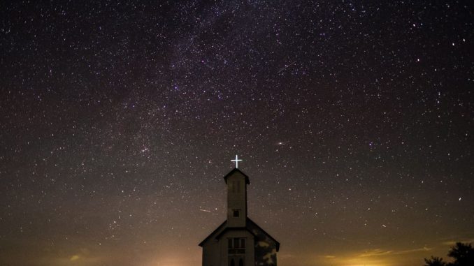 White chapel (call to holiness) under starry sky. Foreground in the dark and glow on the horizon in the background.