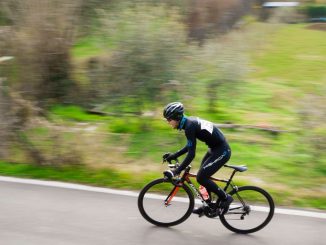 Cyclist dressed in black climbing a moutain road (accept pain) during daytime. Blurred landscape in the background.