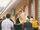 Priest presenting the monstrance to a group of people (know my Son) in front of a brown building during daytime.
