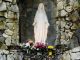 Statue of the Virgin Mary in an alcove of a gray stone wall. Yellow, red and white flowers at the foot of the statue.