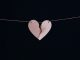Beige broken heart hanging on a wire on black background.
