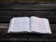 Open Bible on a rustic style dark tea coloured outdoor bench.