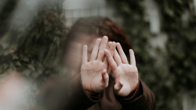 Person in long brown sleeve shirt covering face with the back of the hands. Image is blurry except for hands and sleeves.