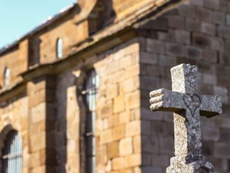 Heart drawn on a gray concrete cross in the foreground. Stone building behind, under a blue sky.