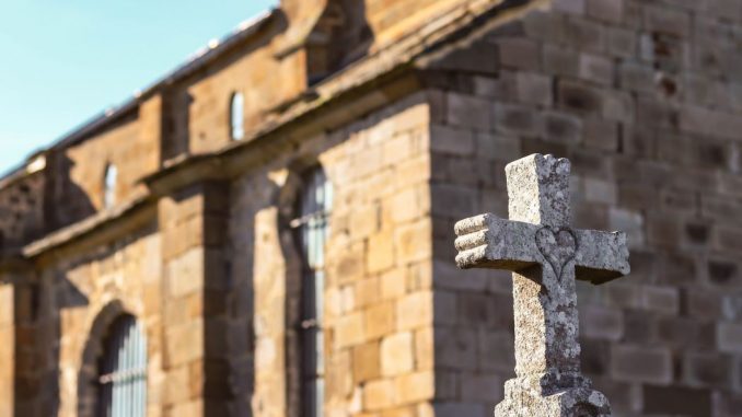 Heart drawn on a gray concrete cross in the foreground. Stone building behind, under a blue sky.