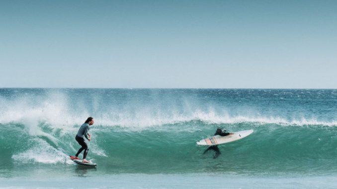 Two men surfing on sea waves during daytime. Sky completely clear.