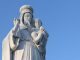 Statue of the Virgin Mary with the baby Jesus in her arms, both dressed in white. Blue sky.