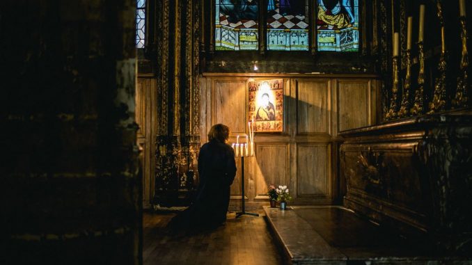 Person praying in front of an illuminated image near a dark brown altar.
