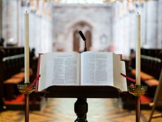Open Bible on a dark brown wooden book stand and a long candle on each side.