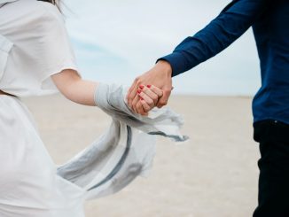 Man and woman holding hands together in field during daytime.