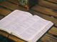 Bible opened on brown wooden table.