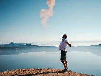 Man standing on sand while spreading arms beside calm body of water.