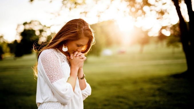 Woman praying beside tree. Blurred image in the background.