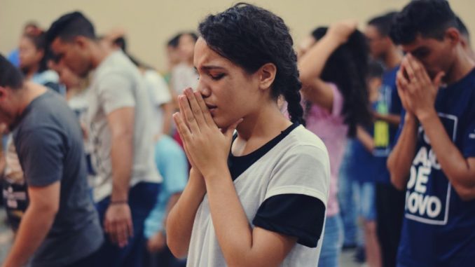 Group of people praying. Woman wearing a white shirt in the foreground.