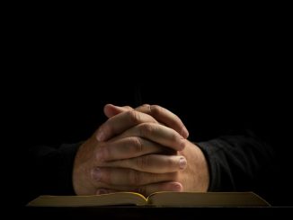 Man praying with folded hands on the Bible.