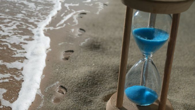 Brown hourglass with blue sand on shore.