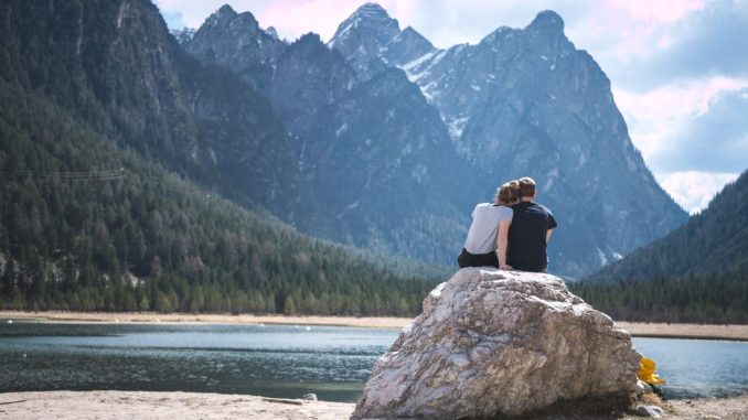 A couple sits on a rock looking out over a lake.