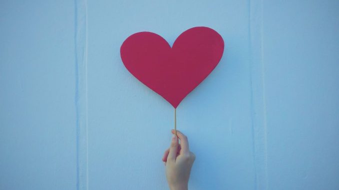 Person holding heart shaped red balloon.