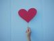 Person holding heart shaped red balloon.
